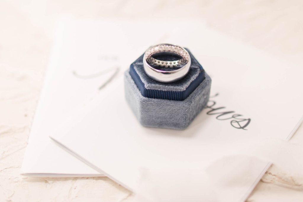 2 gold wedding rings in grey box on top of cream wedding invitations.