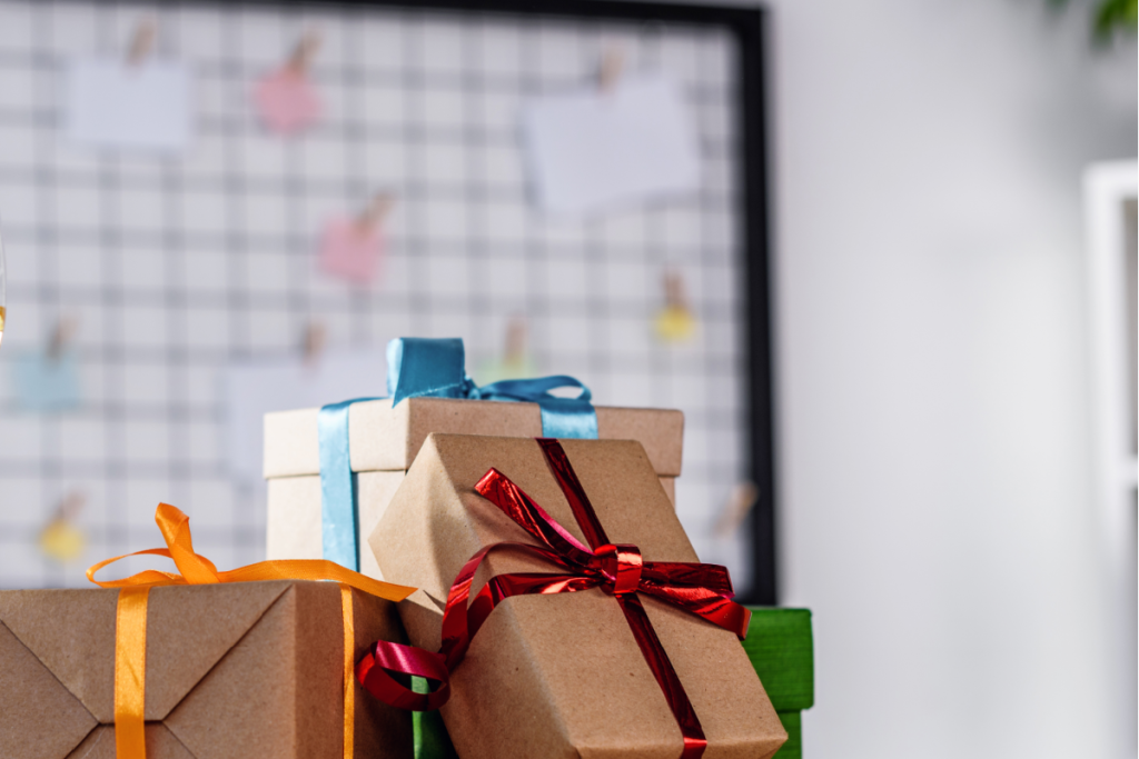 pile of brown paper wrapped gifts in front of an office white board.