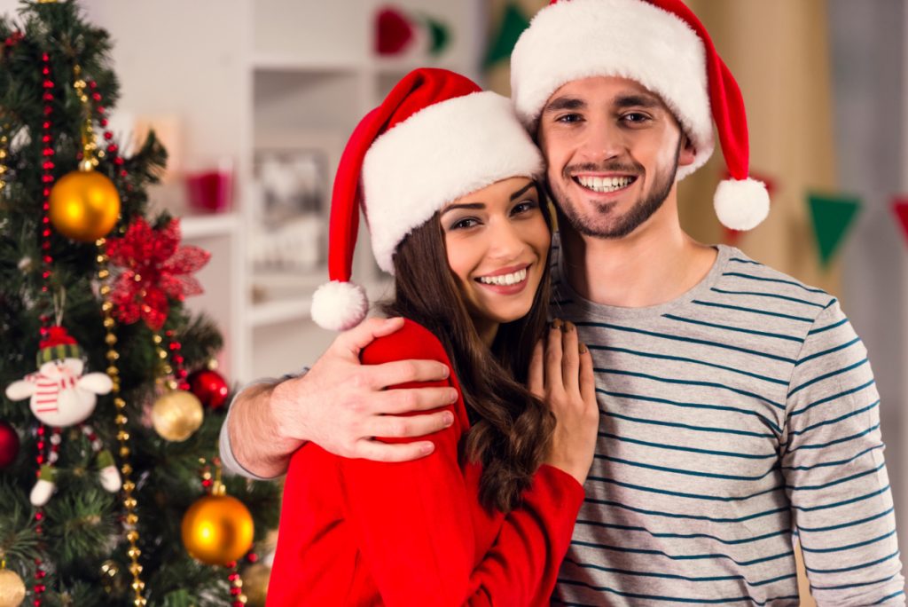 A couple in santa hats posing in front of a christmas tree.
