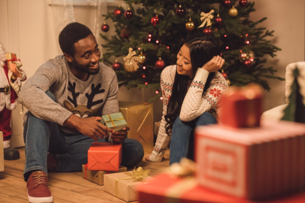 A man and woman sitting on the floor in front of a christmas tree.