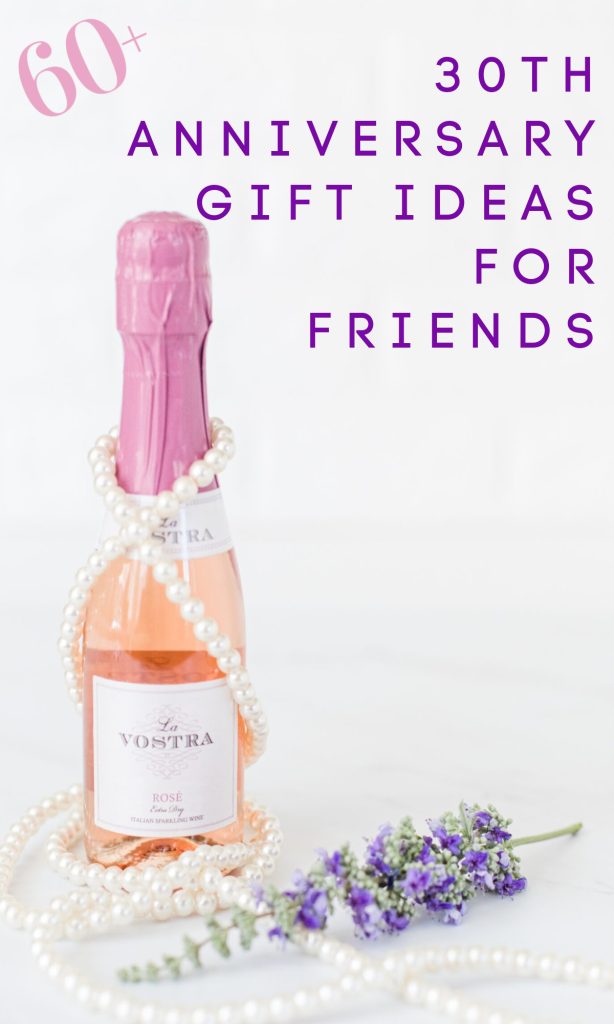 bottle of pink champagne with pearls and next to sprig of purple flowers.