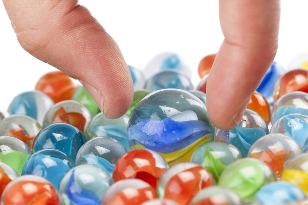 A hand reaching into a bowl of colorful marbles.