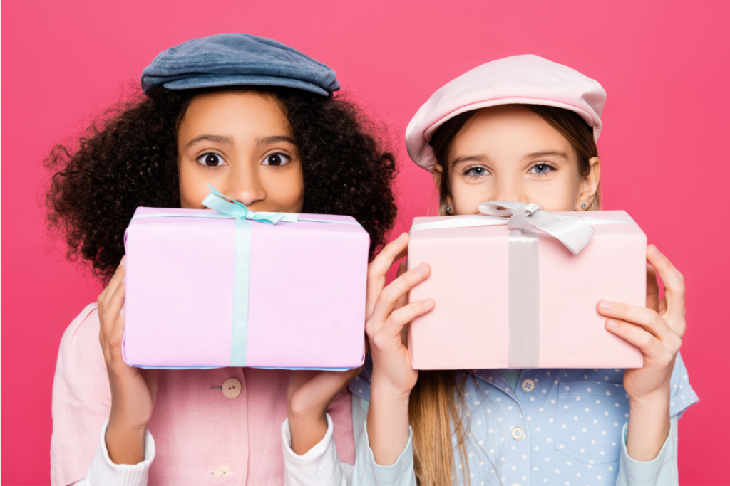 Two little girls holding gift boxes over pink background.